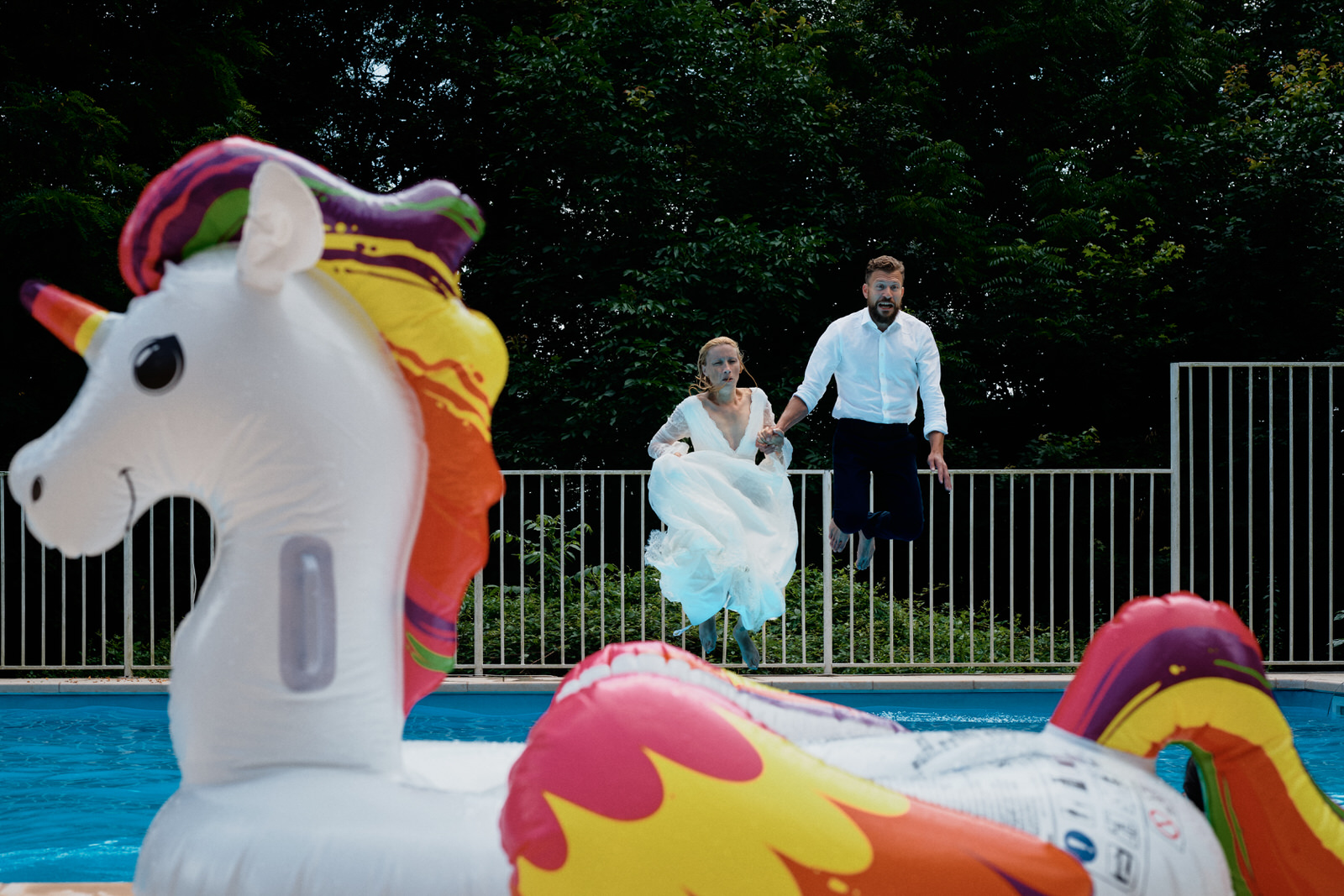 Couple de mariés sautant dans une piscine avec une bouée licorne