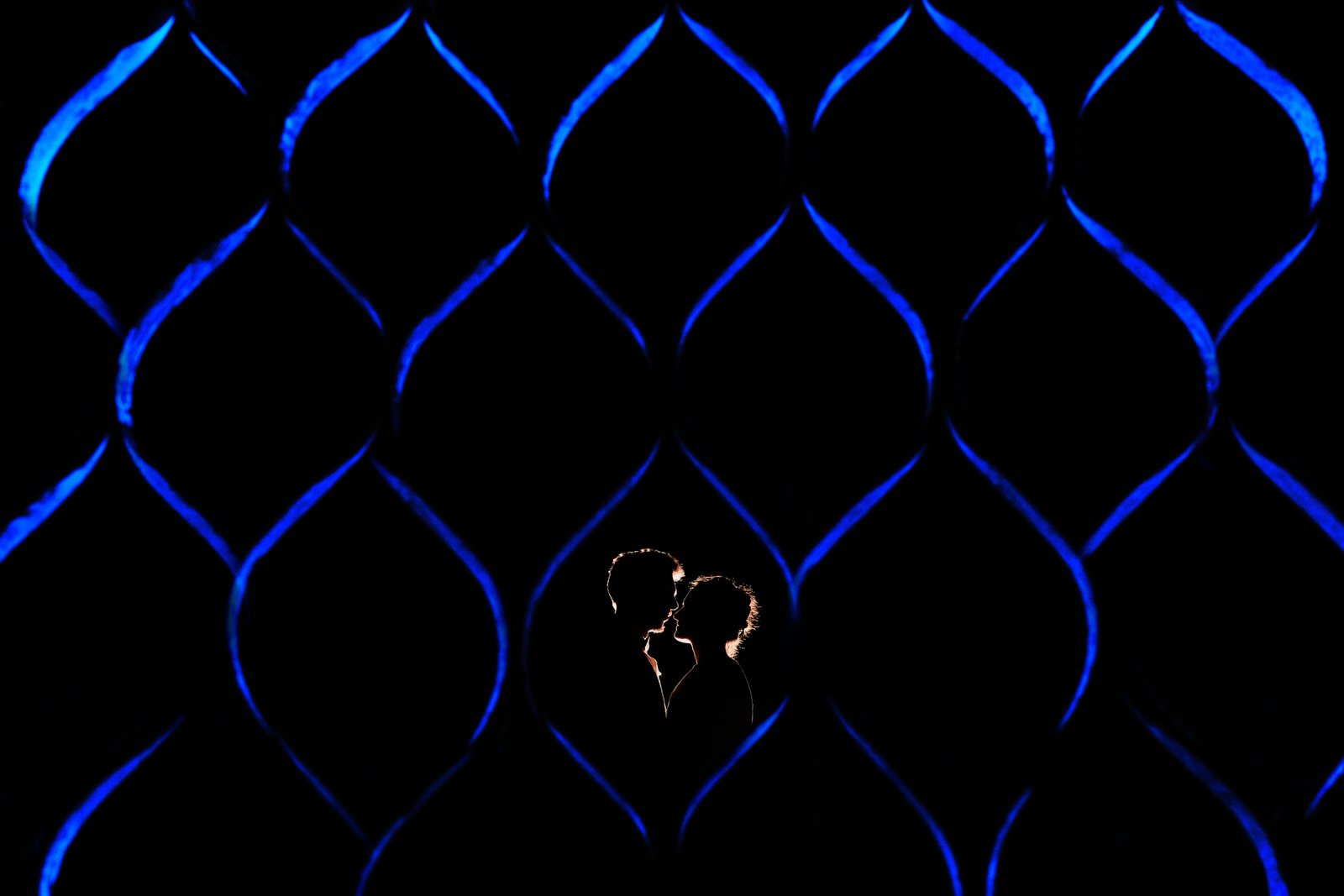 couple face a face en silhouette derrière une barrière éclairée avec des flashs bleus