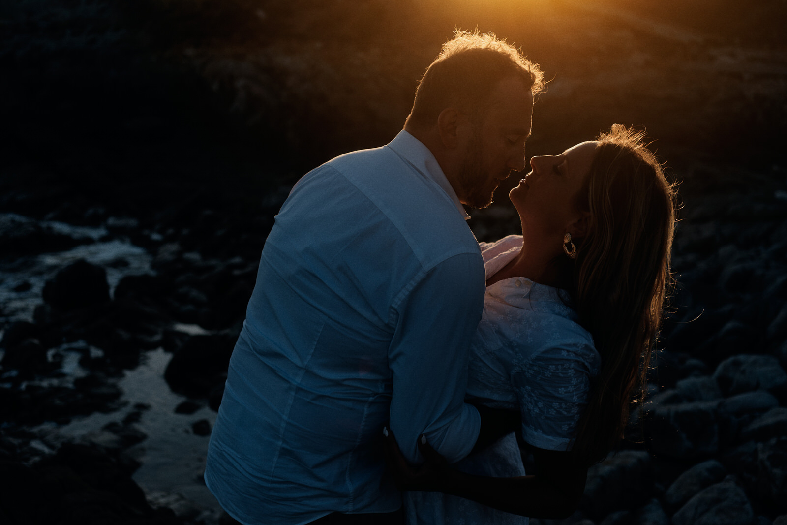 couple posant face à la mer à contre jour au coucher de soleil