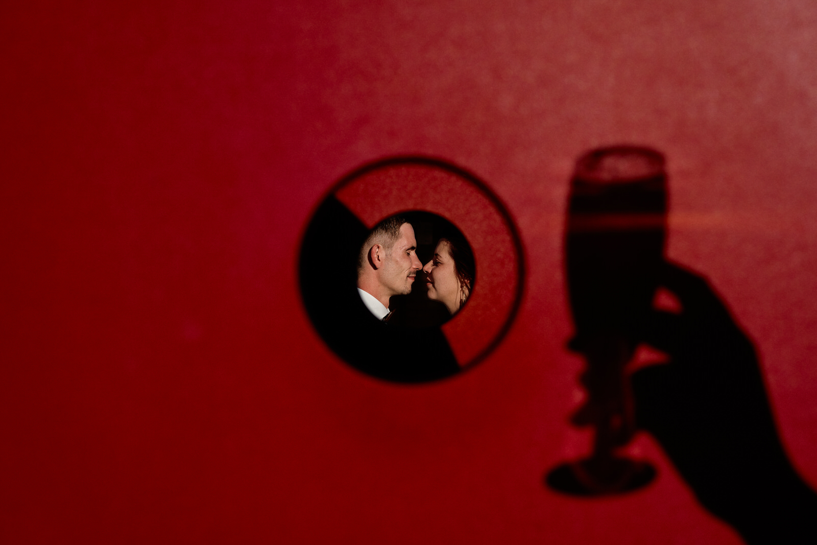 photo de couple au travers un toboggan rouge, on voit l'ombre d'une main qui tient un verre de champagne