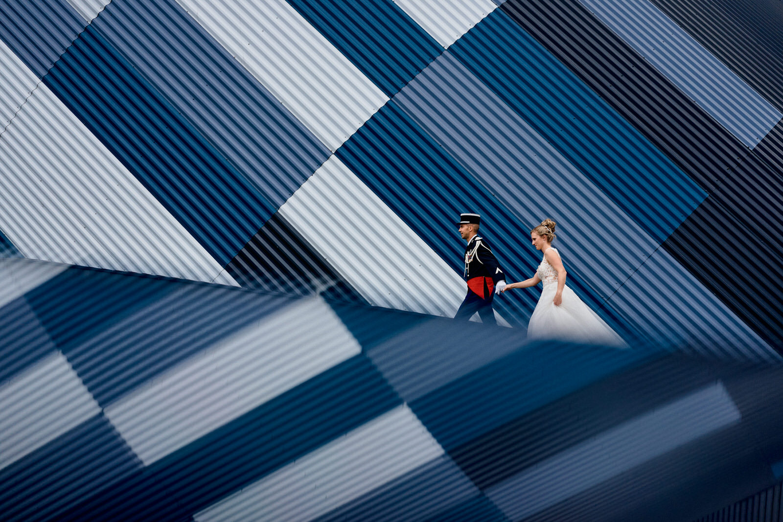 photo de couple des mariés qui marche devant un bâtiment graphique bleu. Le bâtiment est en reflet