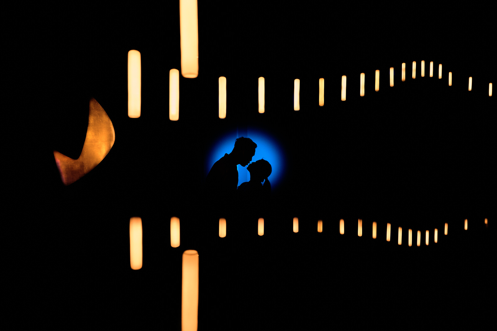 couple qui s'embrasse en silhouette sur un fond bleu derrière un lustre stylé