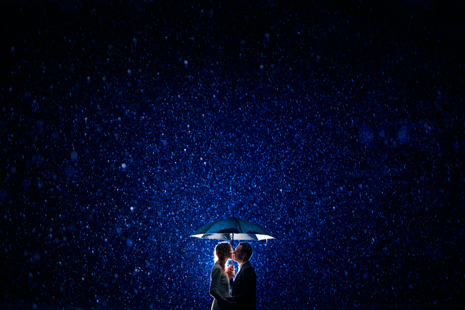 couple qui s'embrasse sous la pluie, sous un parapluie de nuit