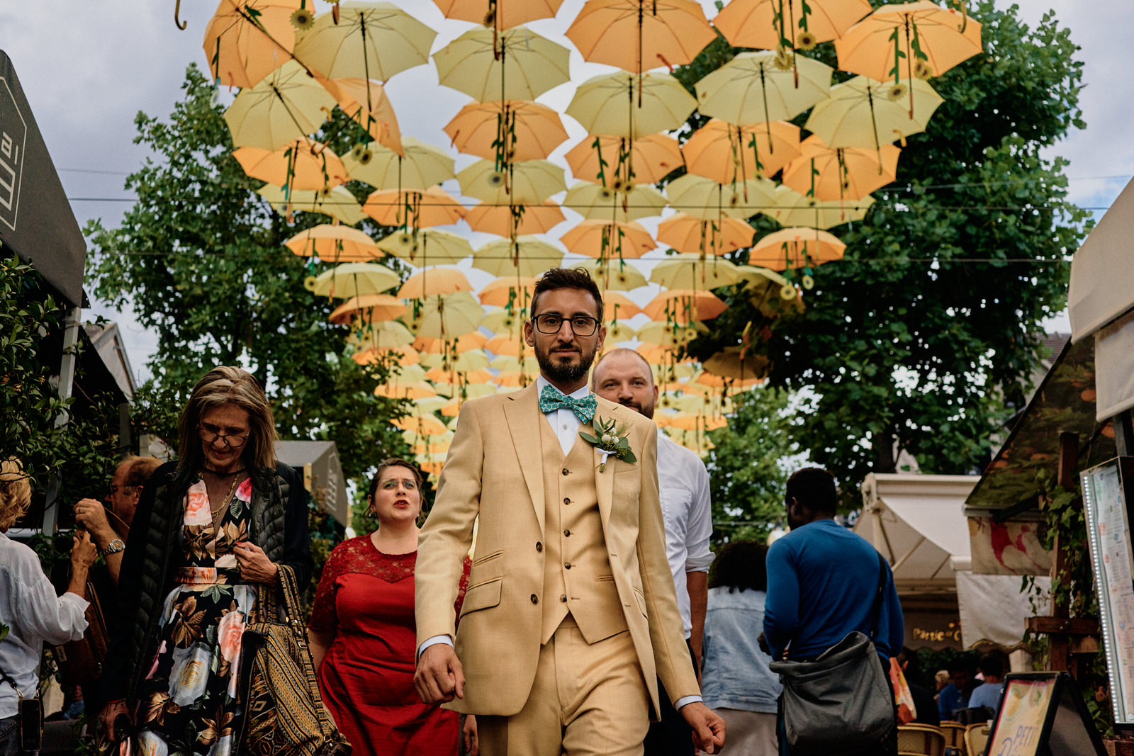 Marié dans un costume jaune marchant sous un ciel de parapluies jaunes