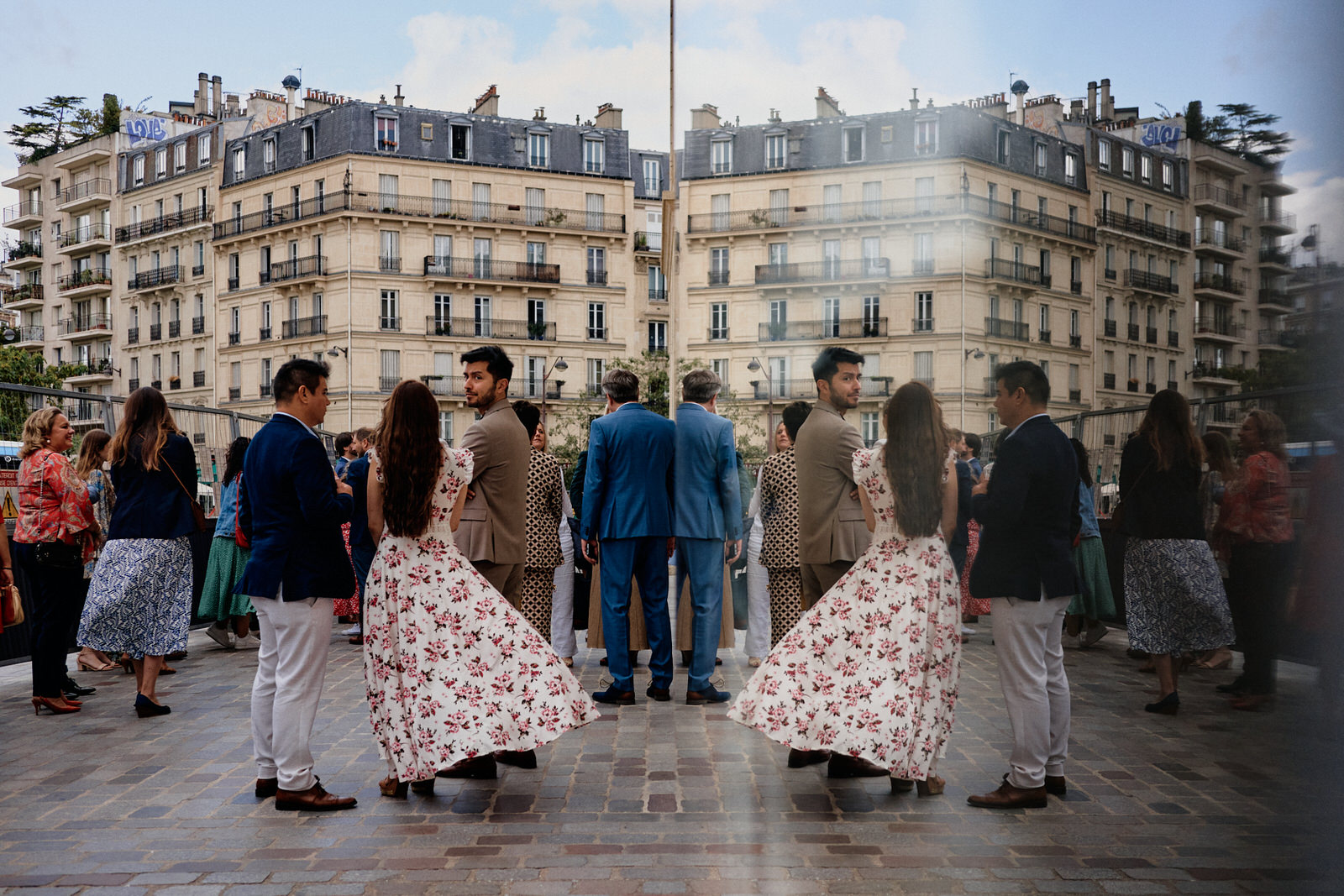 Invités du mariage attendant l'arrivée des mariés devant la mairie du 13ème arrondissement de Paris pendant les travaux. La scène se reflète dans une vitre