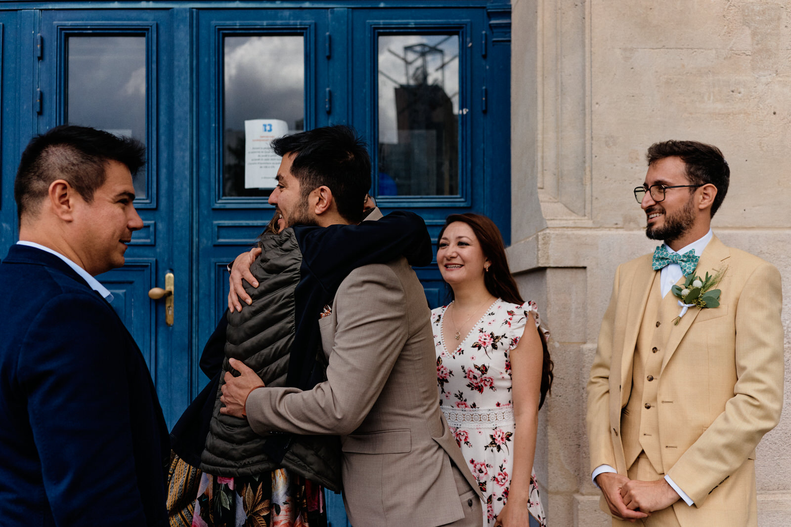 Invités se faisant un câlin sous le regard du marié avant une cérémonie civile à Paris