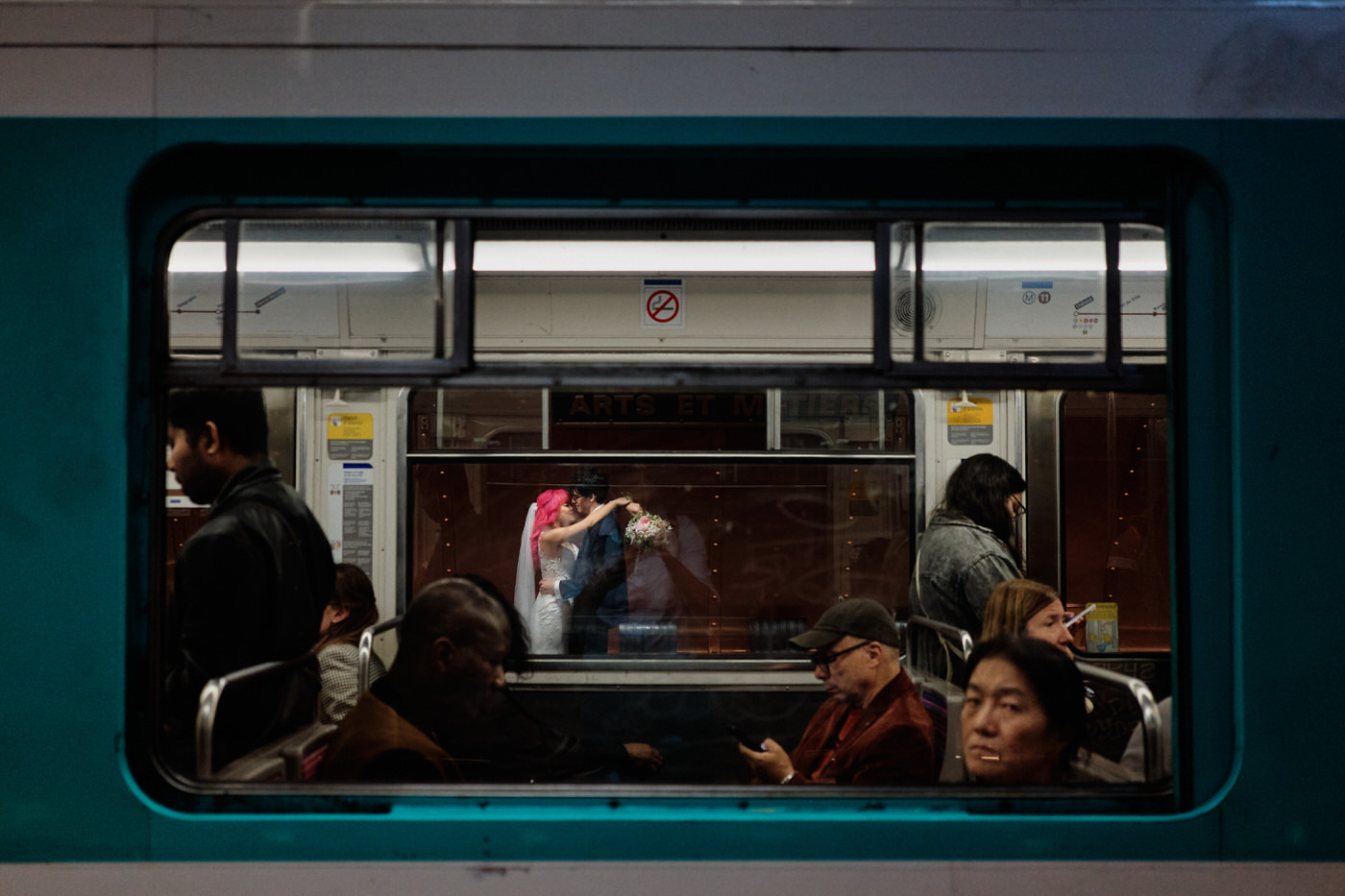 photo de couple prise au travers une rame de métro parisien. On voit les gens dans le métro au premier plan