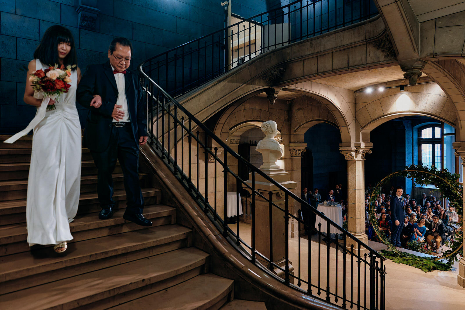 mariée faisant son entrée pendant la cérémonie laique de mariage au bras de son père. On voit aussi sur la photo le marié qui l'attend et les invités qui les regardent