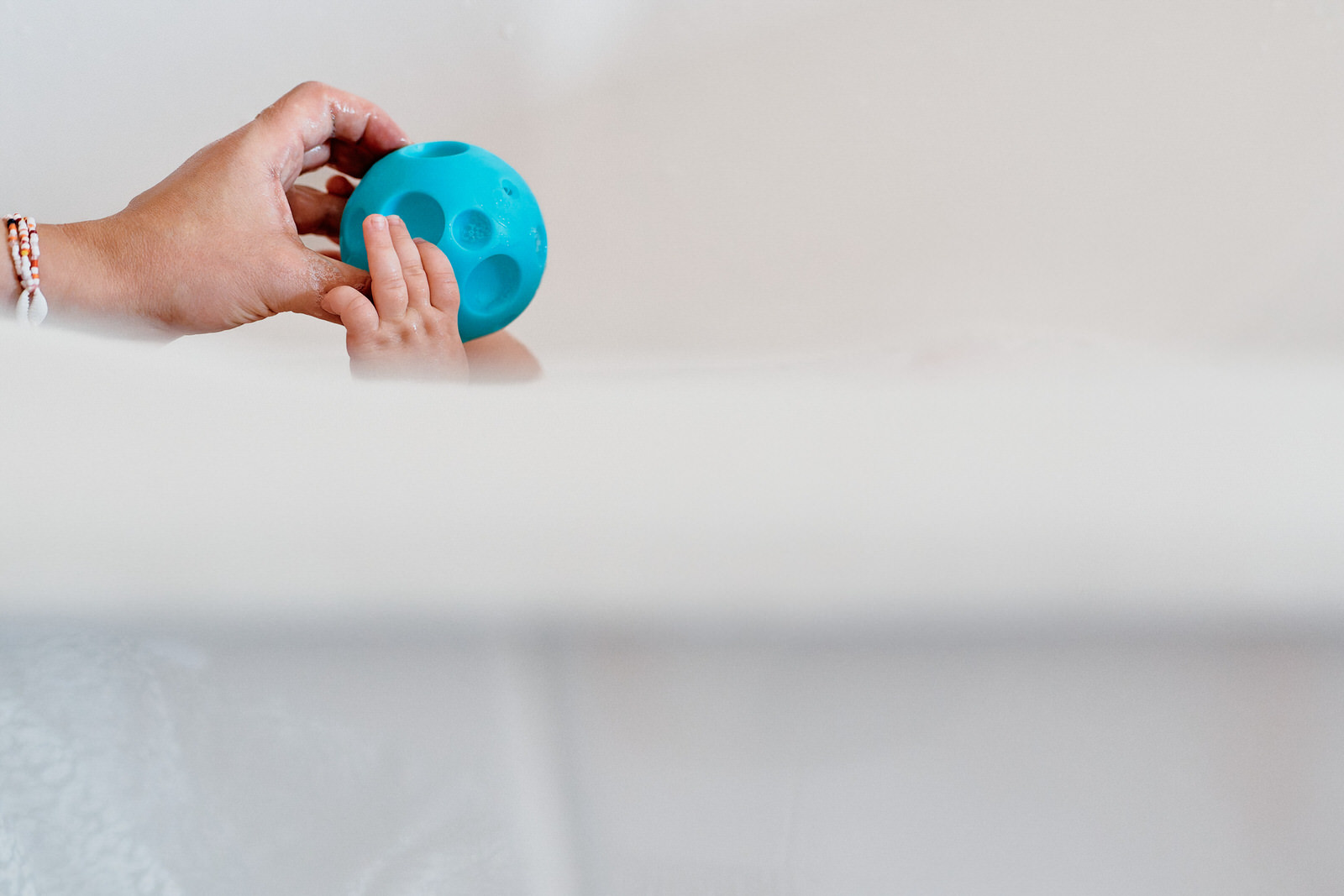 Main d'un bébé dans son bain attrapant un jouet tendu par sa maman