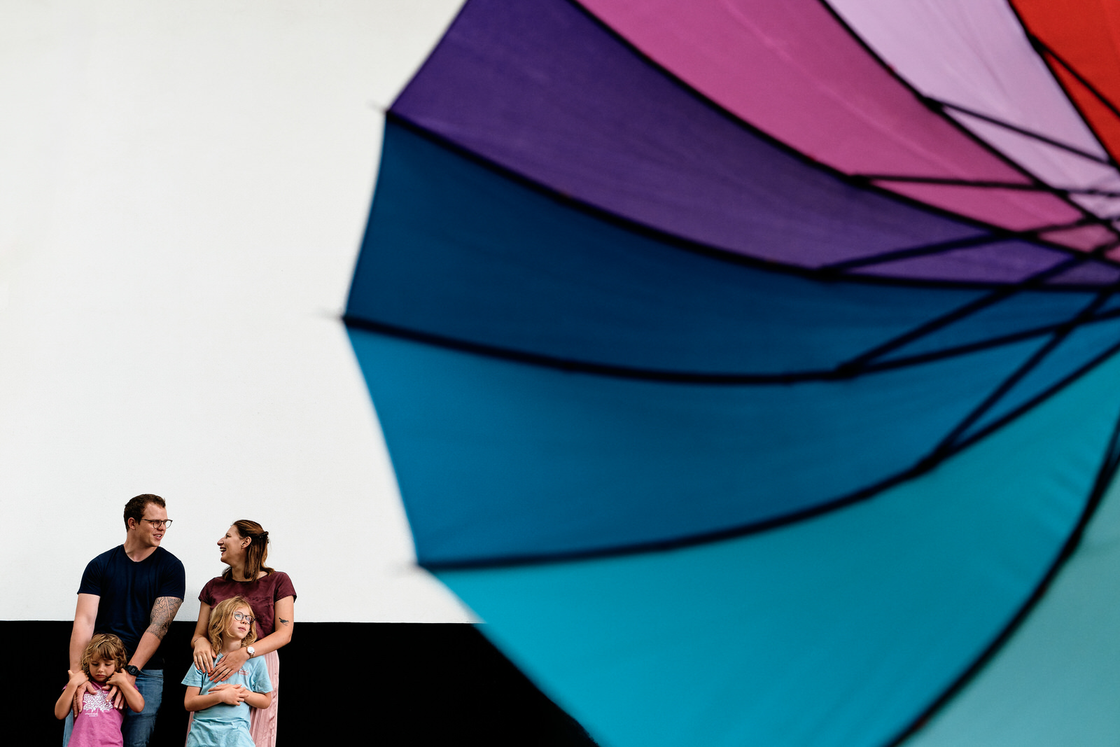 Famille pendant une séance photo lifestyle urbaine, un parapluie coloré au premier plan vient donner un côté très graphique à l'image