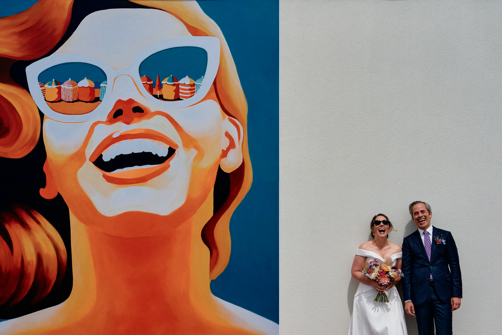 photo d'un couple éclatant de rire devant un mur tagué d'une femme éclatant de rire, prise par des photographes de mariage urbains