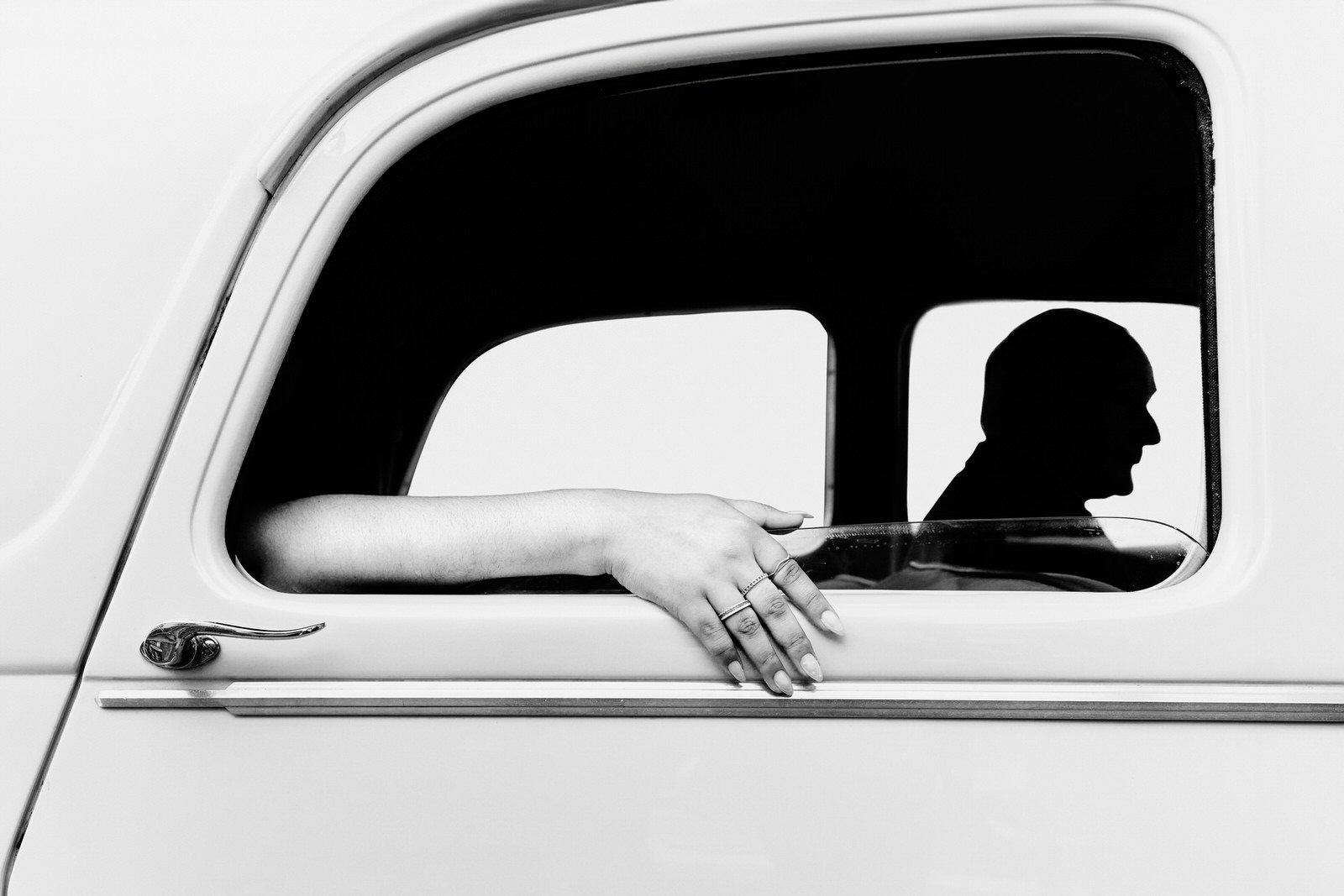 Photo en noir et blanc de la voiture de mariage, on voit la main de la mariée sortant de la fenêtre de la voiture et la silhouette du chauffeur qui rappelle le style de Hitchcock