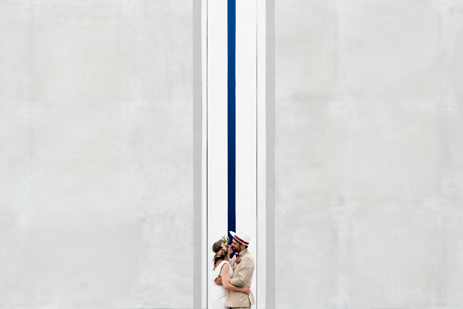 photo de couple de mariés, les mariés en petit dans l'image, deux grands murs blancs, une ligne bleue qui coupe l'image en deux, et les mariés au centre de l'image