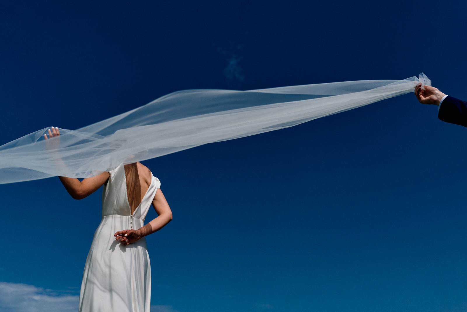 photo de couple de mariés, le marié tient le voile de la mariée qui est de dos