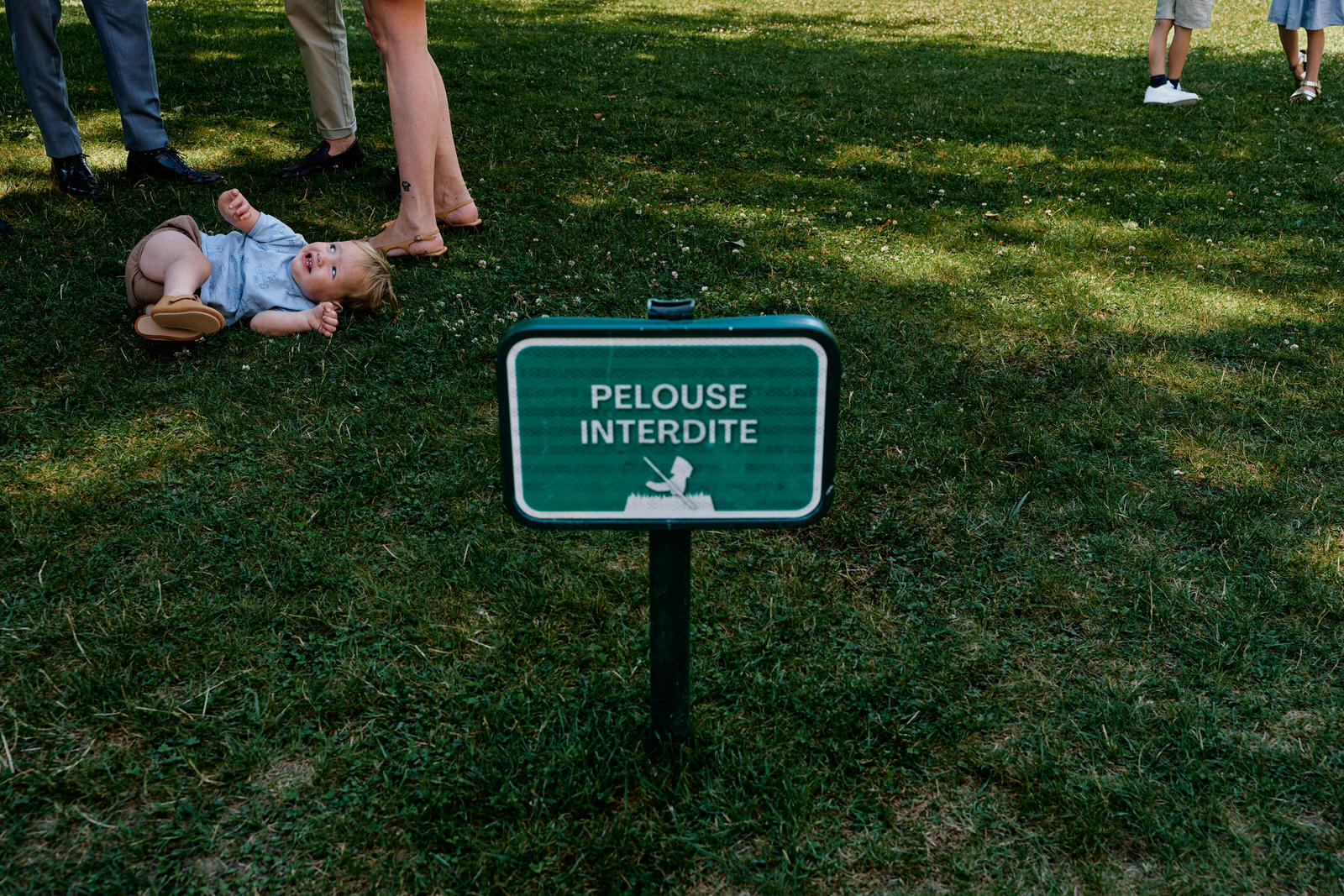 photo humoristique ou un peut lire sur un panneau "pelouse interdite". On voit derrière le panneau plein de pieds qui attentent le début de la cérémonie.