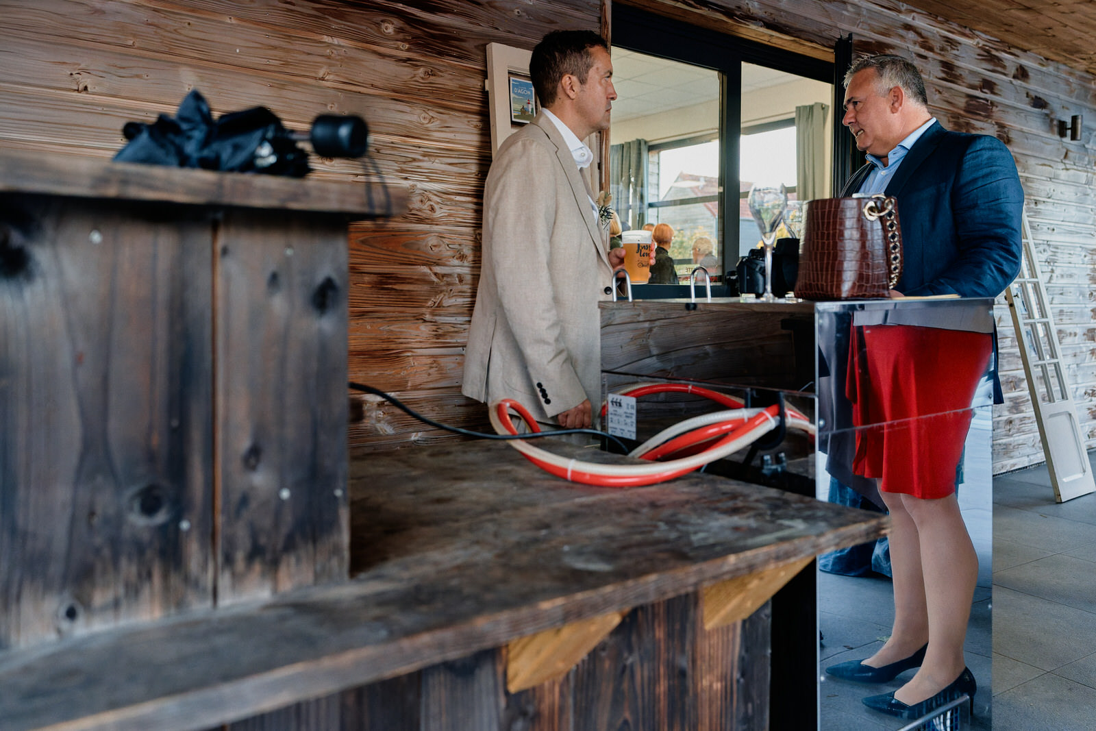 le marié et un invité discutent devant une tireuse à bière. Avec le reflet de la tireuse, l'invité porte une jupe