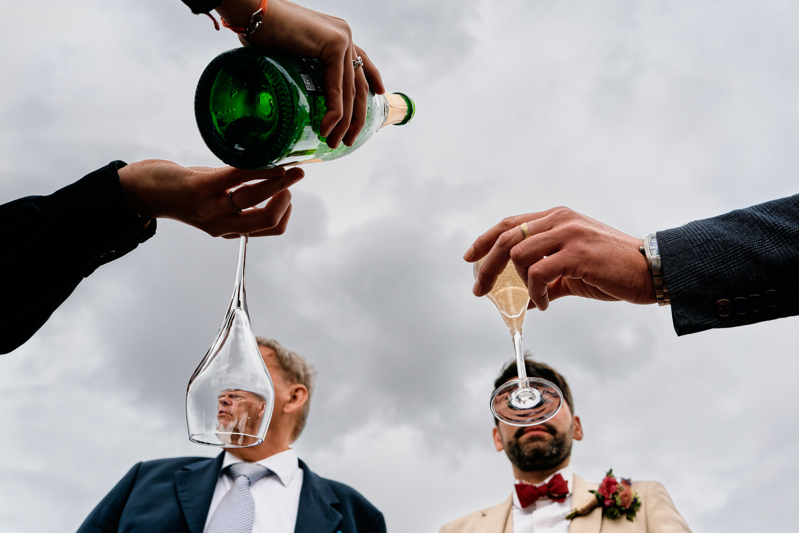 une serveuse sert du champagne à un invité, les tetes du marié en arriere plan sont cachées par 2 verres