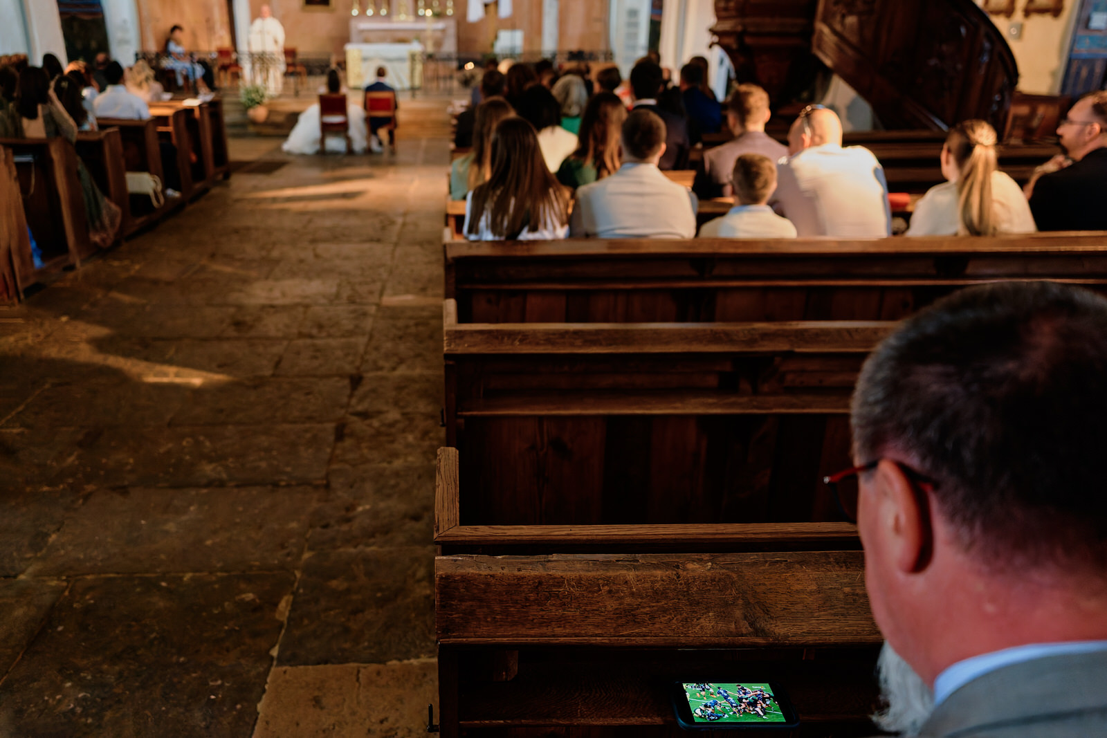 un invité regarde le rugby sur son telephone pendant la messe du mariage